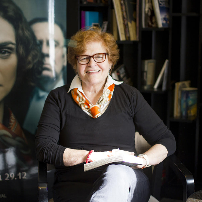 Older woman wearing black dress holding book, sitting down and smiling