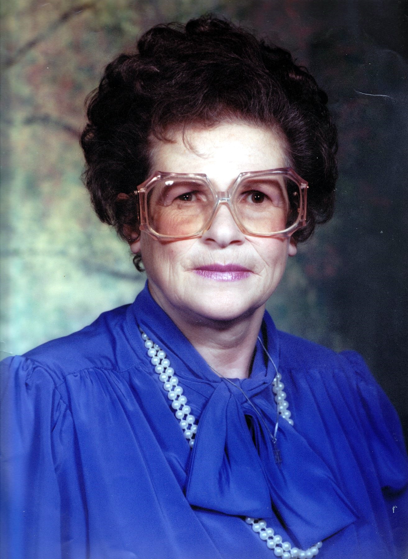 Woman wearing large glasses, pearls, and blouse